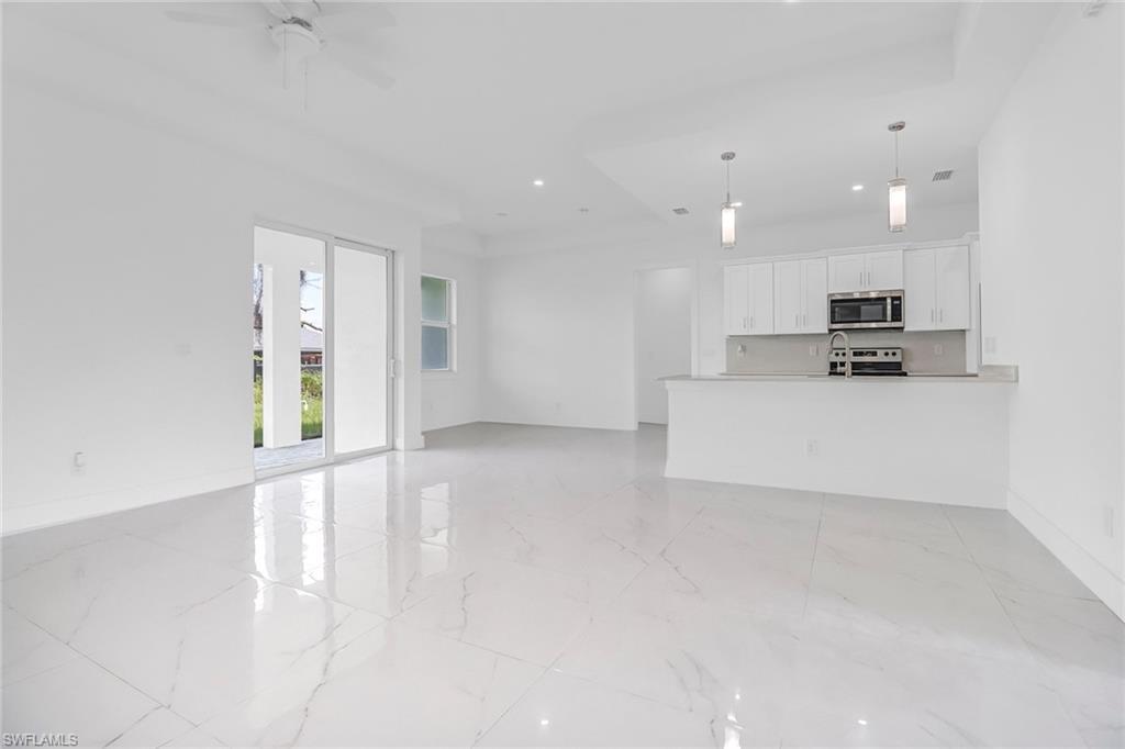 Image 4: Spacious interior featuring white tile flooring throughout, a modern kitchen with white cabinetry and stainless steel appliances, and a ceiling fan