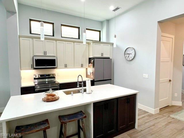 Image 2: Gourmet kitchen featuring a large island with white stone countertops, stainless steel appliances, two-tone cabinetry, and wood-finish flooring