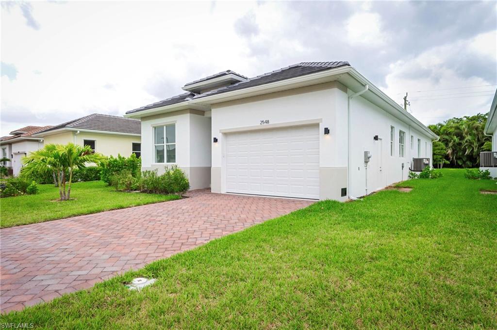 Image 2: View of front facade featuring a front lawn, stucco siding, decorative driveway, a garage, and a tile roof