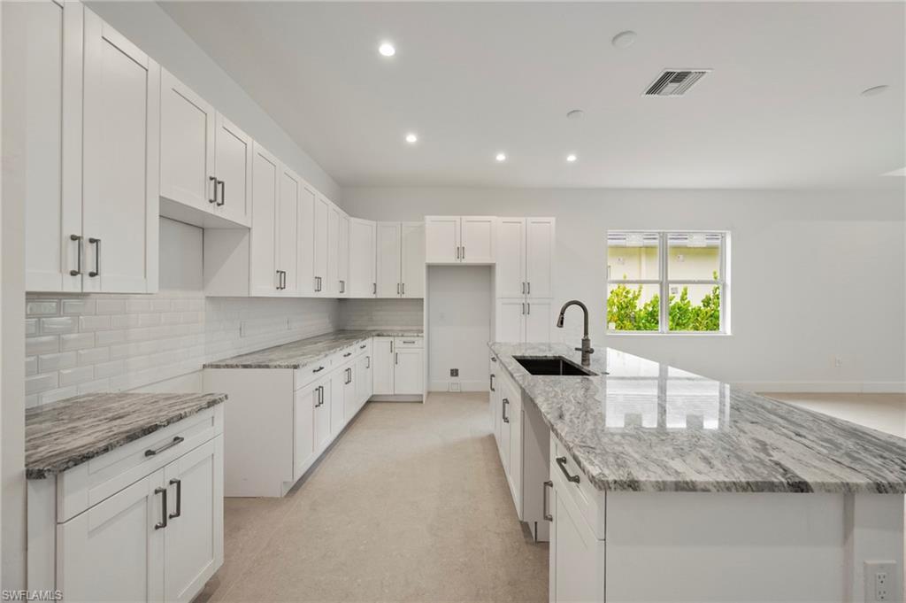 Image 3: Kitchen with white cabinetry, light stone counters, recessed lighting, an island with sink, and backsplash