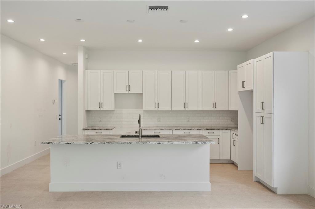 Image 4: Kitchen featuring light stone countertops, white cabinetry, recessed lighting, backsplash, and an island with sink
