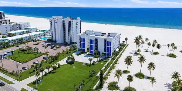 Image 2: Coastal property featuring a white sand beach, expansive blue ocean, and mature palm treesExpansive land parcel with direct beach access, surrounded by established buildings and roadways - Virtually Edited Image