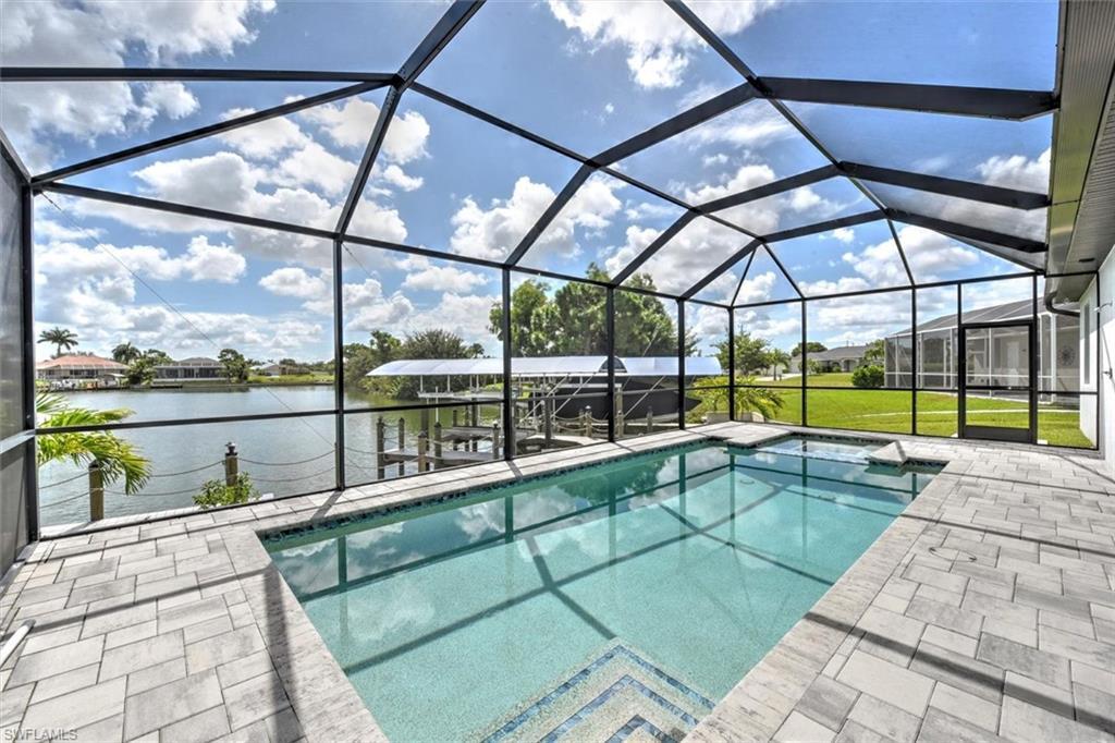 Image 4: Screened outdoor living area featuring a rectangular pool with a spa, paver decking, and waterfront access with a boat dock
