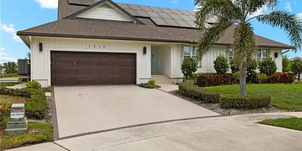 Image 2: View of front of home featuring a shingled roof, driveway, roof mounted solar panels, a garage, and a front lawn
