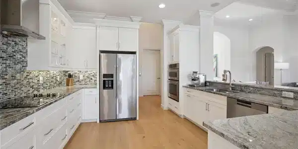 Image 3: The kitchen has stainless steel appliances, spacious  counter space, white cabinets, attractive backsplash, and wood floor