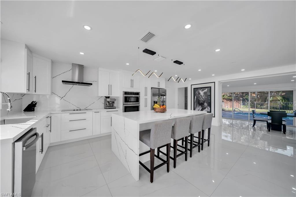 Image 4: Kitchen featuring light stone countertops, a kitchen island, white cabinets, stainless steel appliances, and a kitchen bar