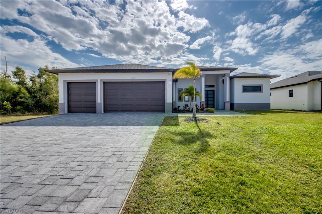 Image 1: Prairie-style home with decorative driveway, a front lawn, stucco siding, and an attached garage