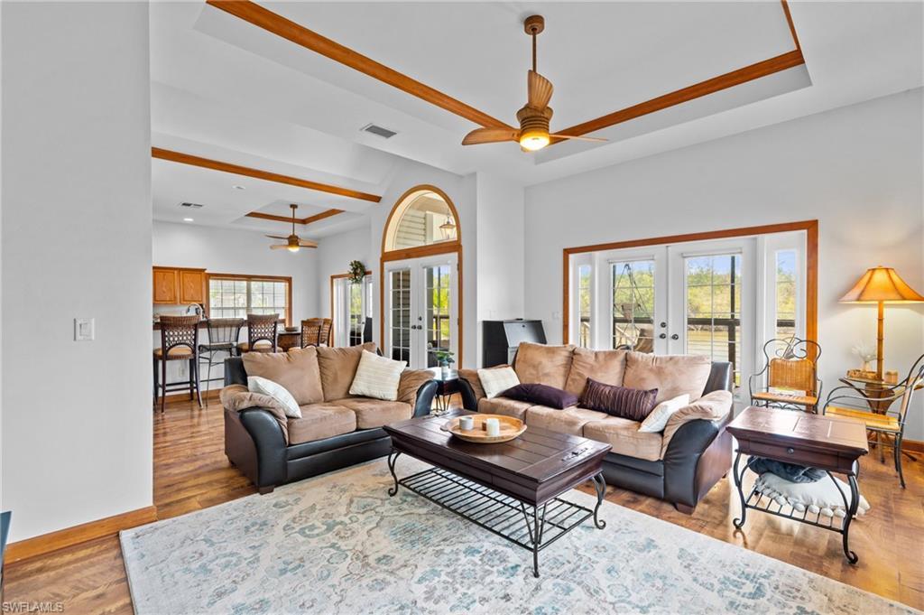 Image 2: Living room featuring visible vents, ceiling fan, a tray ceiling, wood finished floors, and french doors