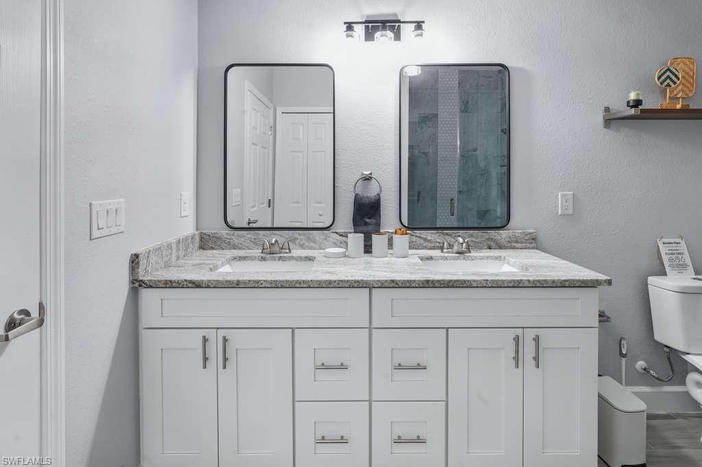 Image 3: Bathroom featuring double vanity, a textured wall, and a stall shower