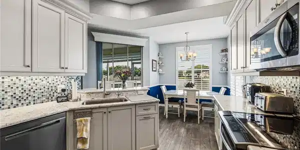 Image 3: A beautifully redesigned kitchen overlooking the tranquil lake, showcasing exquisite blue-veined granite countertops and matching backsplash, enhanced by ambient under-cabinet lighting, recessed illumination, and a suite of premium stainless steel appliances.