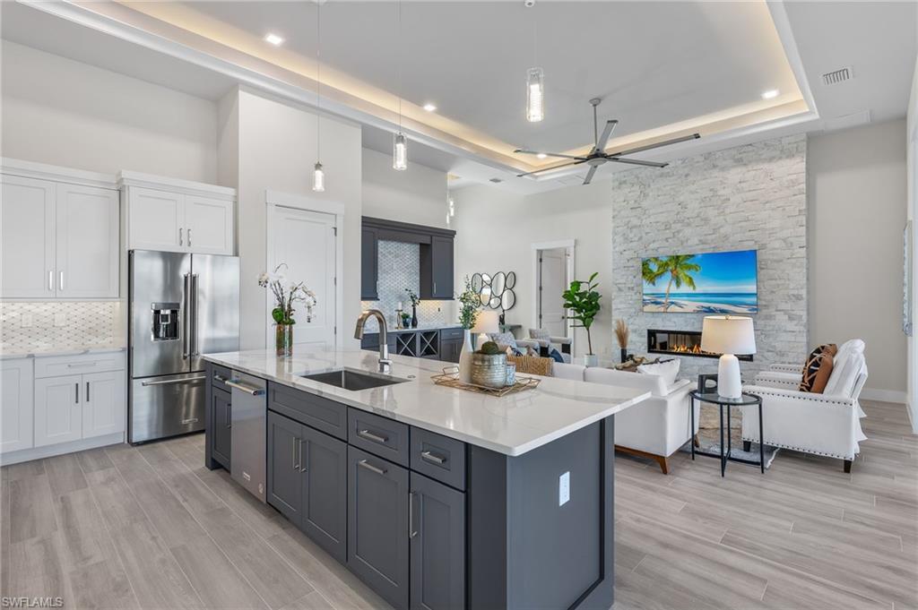Image 4: Kitchen with white cabinetry, sink, hanging light fixtures, high end refrigerator, and a center island with sink