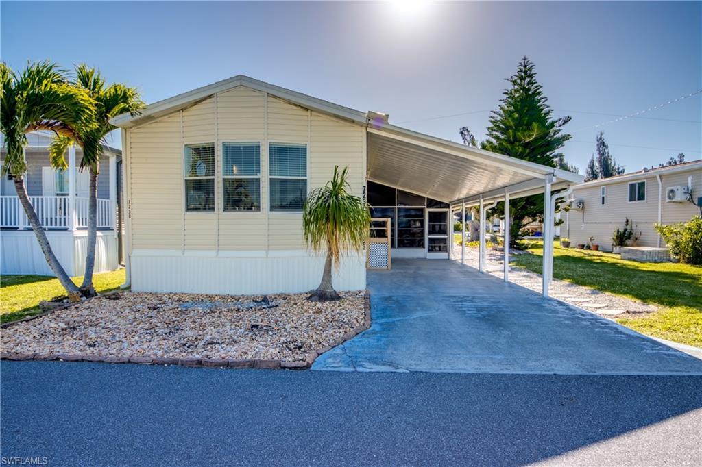 Image 2: The property features a carport, a rock garden with palm trees, and light-colored siding