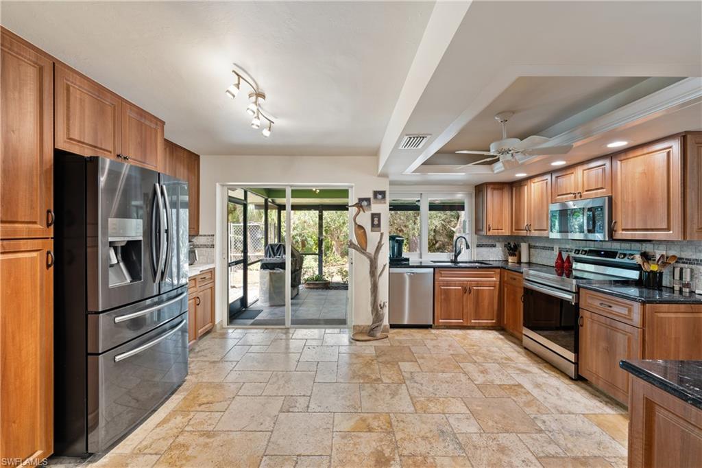 Image 2: Kitchen with stainless steel appliances, ceiling fan, wood finish cabinetry, dramatic stone counters, and stone tile floors