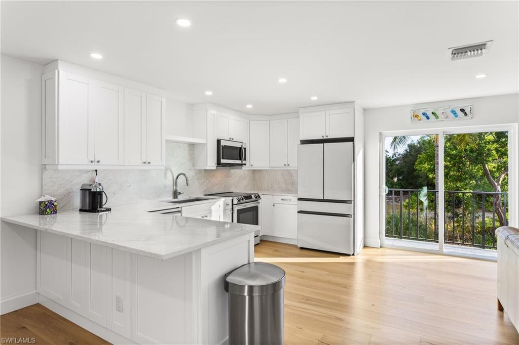 Image 4: Kitchen featuring white cabinets, stainless steel appliances, a peninsula, light stone counters, and light wood flooring