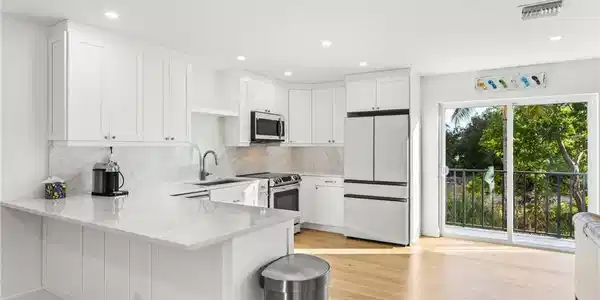 Image 4: Kitchen featuring white cabinets, stainless steel appliances, a peninsula, light stone counters, and light wood flooring