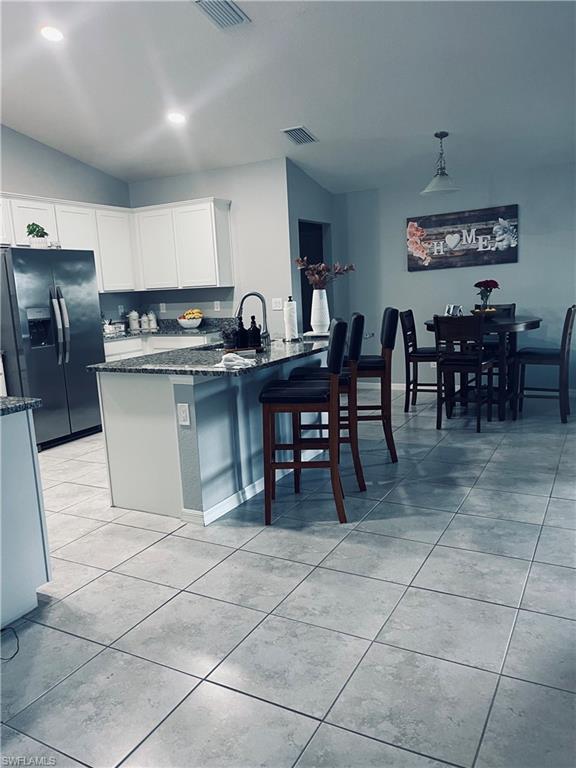 Image 4: Kitchen with refrigerator with ice dispenser, dark stone countertops, a breakfast bar area, a peninsula, and pendant lighting