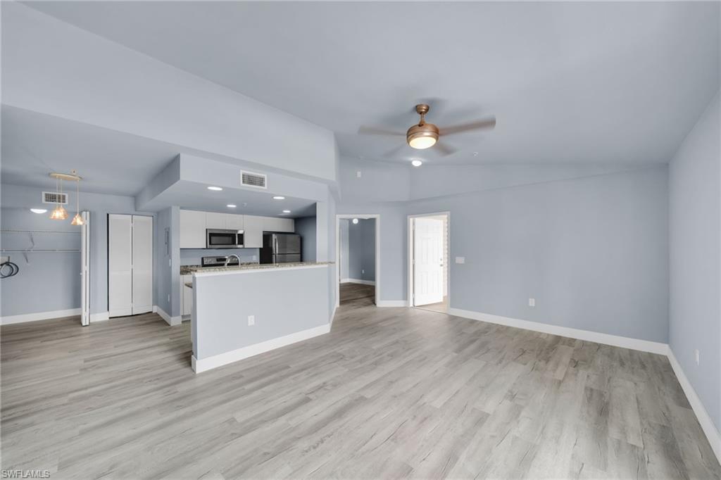 Image 1: Open-concept living area featuring wood-finish flooring, a contemporary ceiling fan, and a kitchen with stainless steel appliances