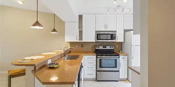 Image 2: Kitchen featuring light tile patterned floors, white cabinets, stainless steel appliances, hanging light fixtures, and tasteful backsplash