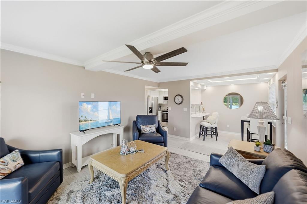 Image 4: Open-concept living area featuring tray ceilings with crown molding, a ceiling fan with light fixture, tile flooring, and a breakfast bar with seating