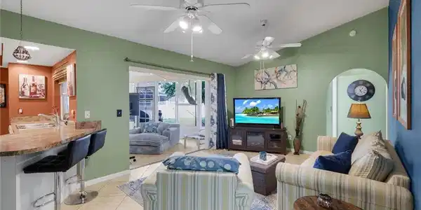 Image 4: Bright, open-concept living room with vaulted ceilings, tile flooring, breakfast bar seating, and sliding glass doors leading to the screened lanai.