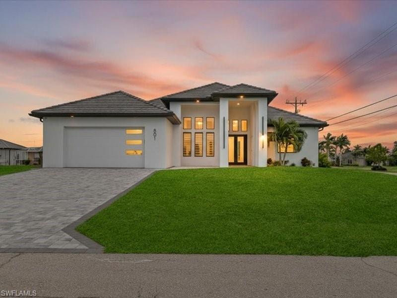 Image 1: View of front facade featuring a yard, decorative driveway, stucco siding, a garage, and a tile roof