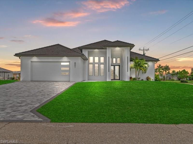 Image 2: View of front of house featuring a front lawn, decorative driveway, stucco siding, and an attached garage