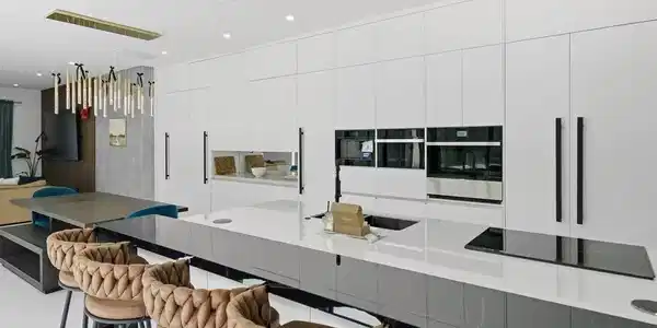 Image 3: Spacious kitchen featuring a large central island with integrated cooktop and sink, sleek white cabinetry with long black pull handles, and built-in stainless steel appliances