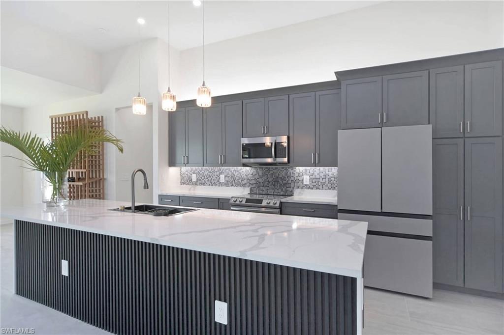 Image 4: Modern kitchen featuring a large island with a white countertop and fluted paneling, gray cabinetry, stainless steel appliances, and pendant lighting