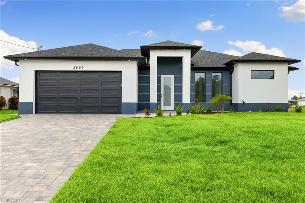 Image 1: Prairie-style home featuring stucco siding, a front lawn, decorative driveway, and an attached garage