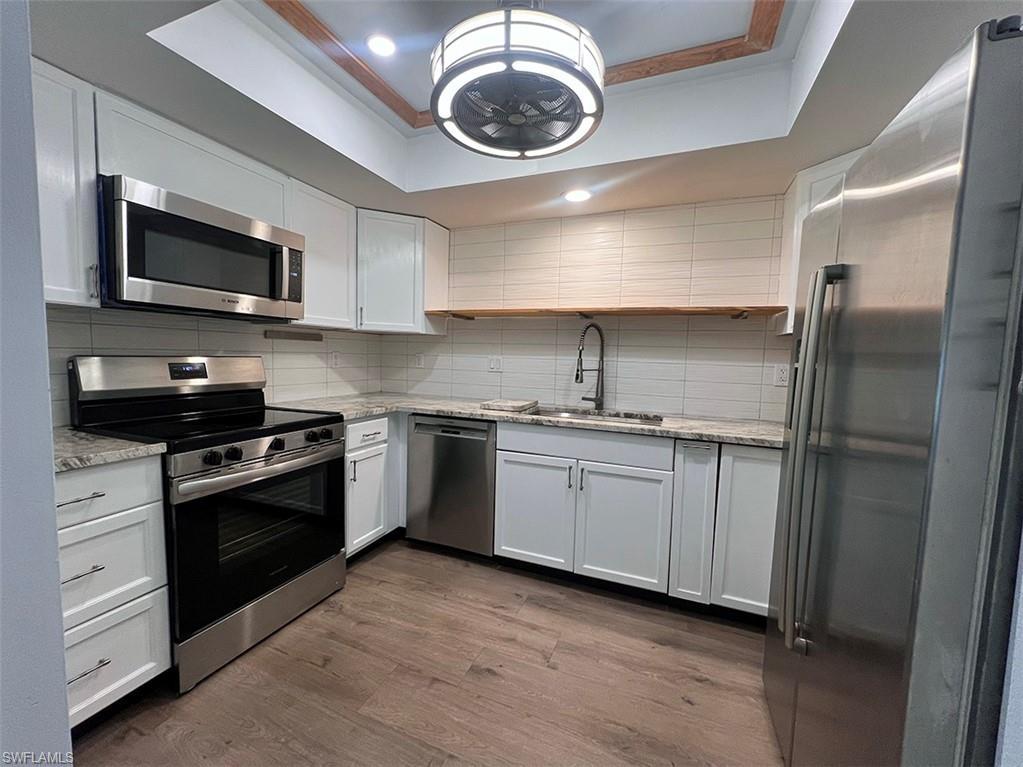Image 1: Kitchen with stainless steel appliances, light stone counters, white cabinetry, a tray ceiling, and dark wood finished floors