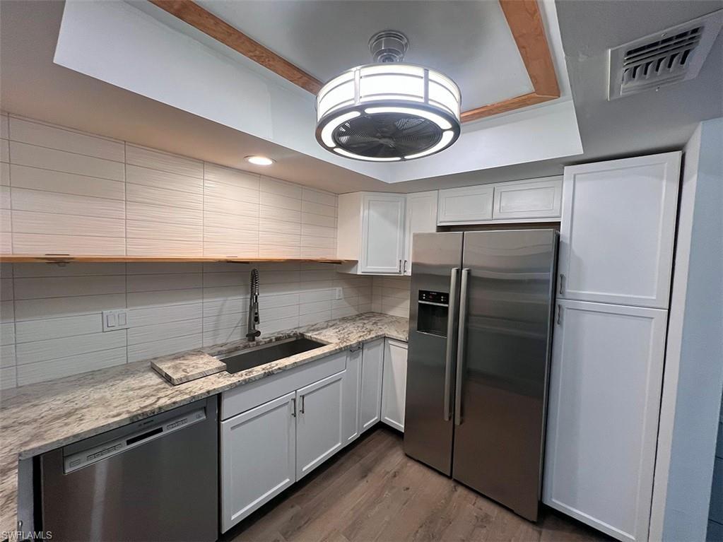Image 3: Kitchen featuring stainless steel appliances, light stone counters, dark wood-style flooring, white cabinetry, and backsplash