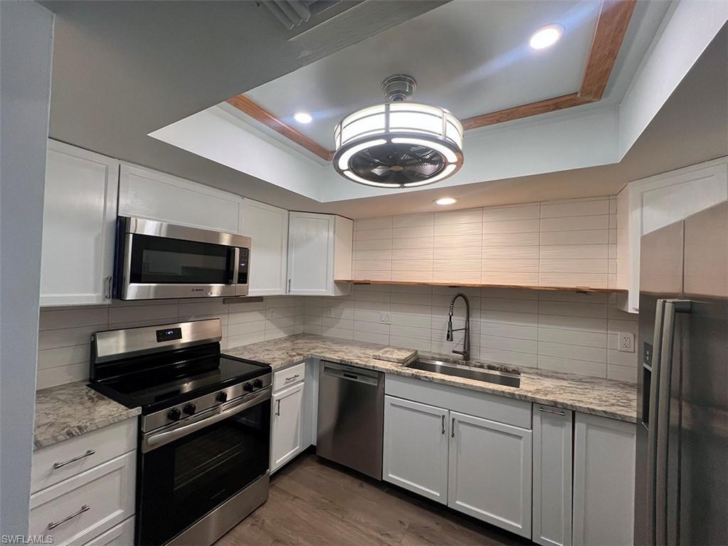 Image 4: Kitchen with stainless steel appliances, ornamental molding, a raised ceiling, light stone countertops, and dark wood-style flooring