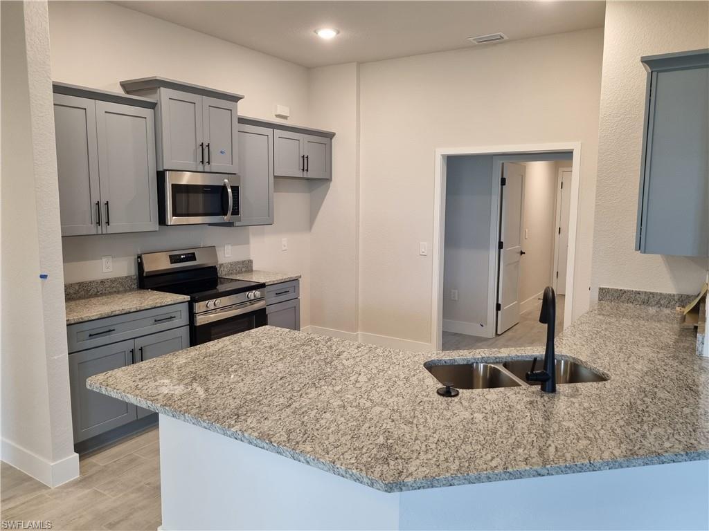 Image 3: Kitchen featuring gray cabinets, stainless steel appliances, a peninsula, light stone countertops, and light wood finished floors