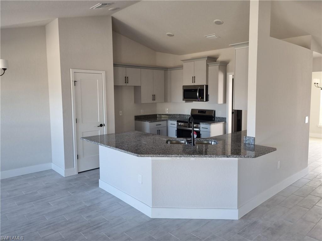 Image 4: Kitchen with dark stone counters, stainless steel appliances, a peninsula, wood tiled floors, and vaulted ceiling