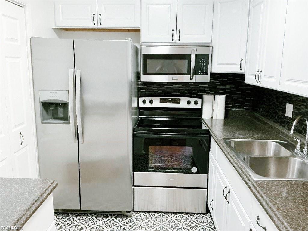 Image 3: Full kitchen featuring white cabinetry with dark hardware, stainless steel appliances, dark countertops, and a mosaic tile backsplash