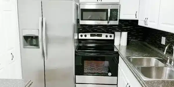 Image 3: Full kitchen featuring white cabinetry with dark hardware, stainless steel appliances, dark countertops, and a mosaic tile backsplash