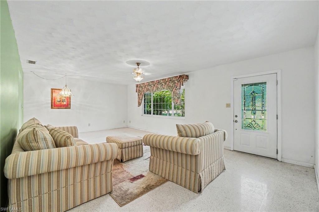 Image 3: Bright living space featuring a decorative glass-paneled entry door, a large window with exterior greenery visible, and a ceiling fan with light fixture
