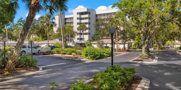 Image 2: Expansive community grounds featuring a multi-story building, mature trees, manicured landscaping, paved roadways, and dedicated parking areas