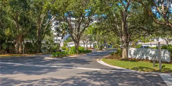 Image 3: Paved community entrance featuring mature trees, landscaped islands, and a prominent "NAPLES COVE" monument sign