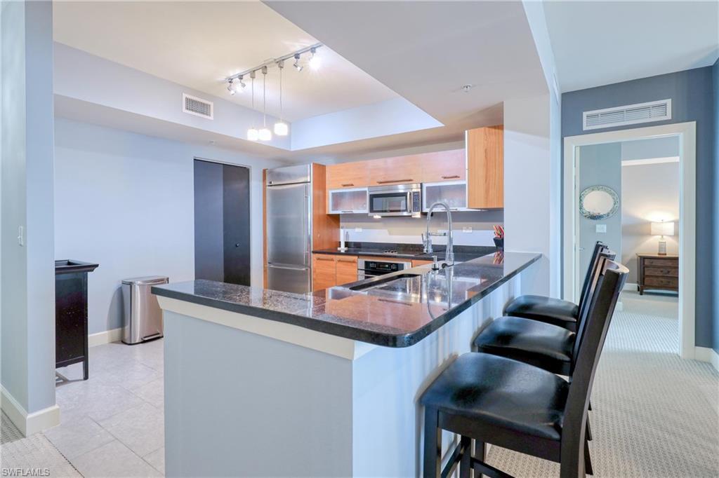Image 4: Kitchen with kitchen peninsula, hanging light fixtures, stainless steel appliances, light brown cabinetry, and a breakfast bar