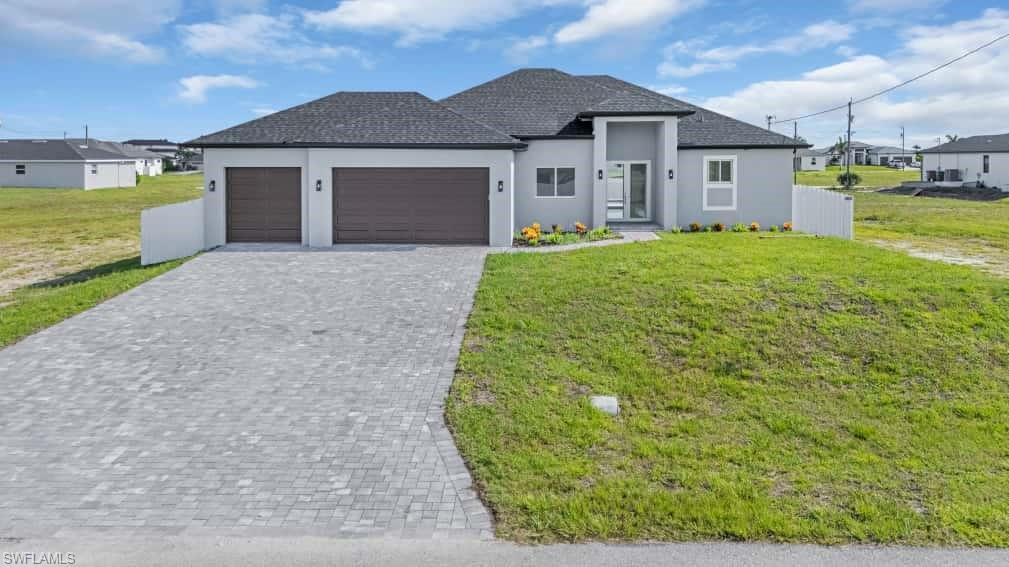 Image 1: View of front of house with stucco siding, a garage, decorative driveway, a front lawn, and roof with shingles
