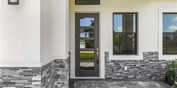 Image 4: Doorway to property featuring stone siding, a patio, and stucco siding