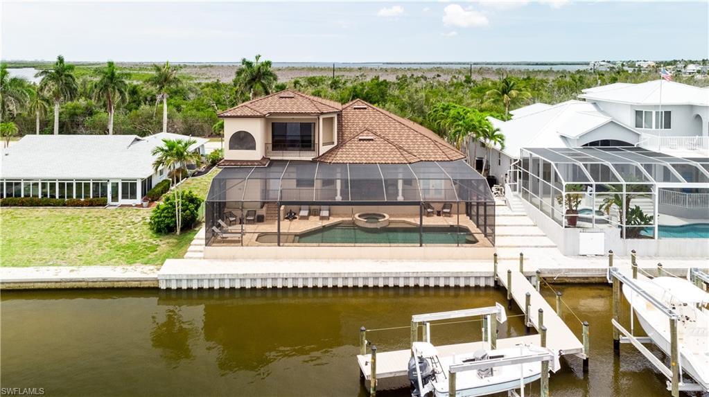 Image 4: Waterfront property featuring a screened-in pool area with integrated spa, a private dock with boat lift, and a tiled metal roof
