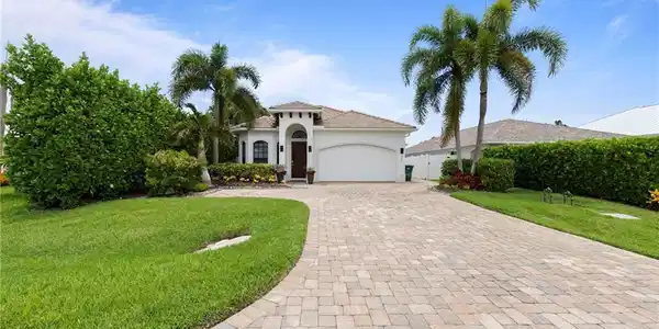 Image 2: Front exterior featuring a white stucco facade, arched entryway, and a paver driveway