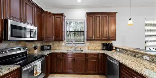 Image 4: Kitchen featuring wood cabinetry, stainless steel appliances, granite countertops, and a tile backsplash