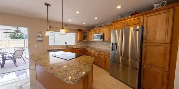Image 3: Kitchen featuring stainless steel appliances, wood finish cabinetry, dark stone counters, hanging light fixtures, and tasteful backsplash