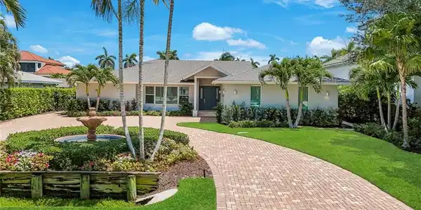 Image 4: Contemporary stucco exterior with a brick paver driveway, a central water feature, and mature palm trees