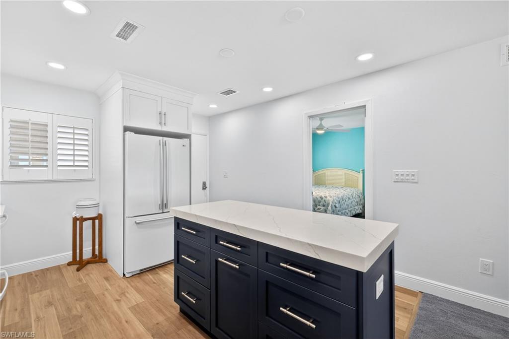 Image 3: Two tone kitchen with freestanding refrigerator, light stone countertops, a kitchen island, light wood-type flooring, and two tone cabinets