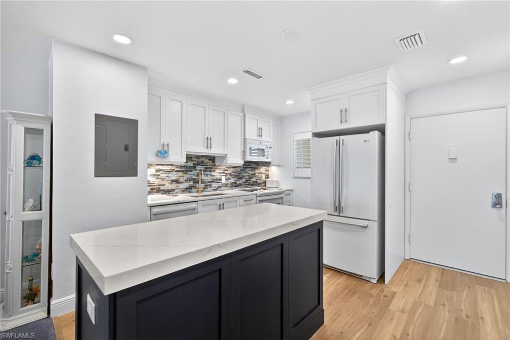 Image 4: Two tone kitchen with light wood-style floors, white appliances, electric panel, backsplash, and two tone cabinetry