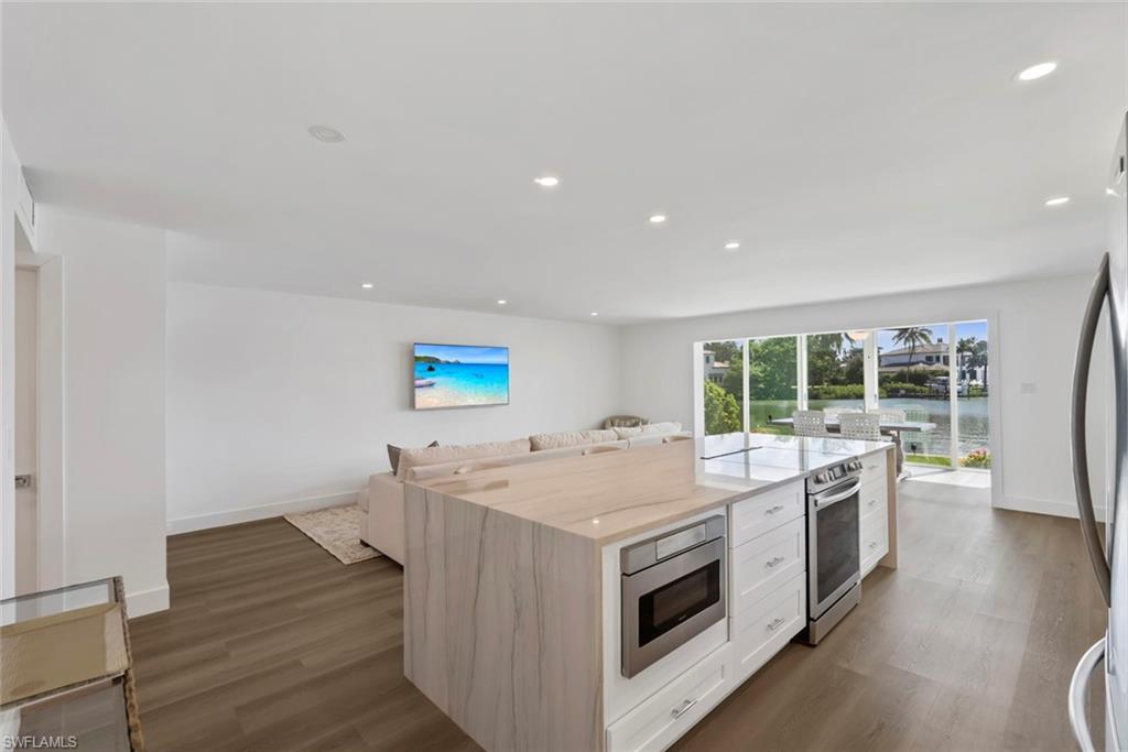 Image 3: Open-concept living space featuring a modern kitchen island with waterfall countertop, integrated microwave, and stainless steel range